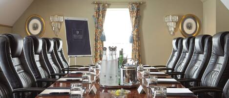 A conference room with a long table, black leather chairs, and a chandelier.