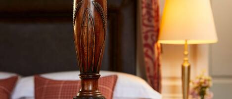 Uma cama com cabeceira de madeira, abajur e mesa de cabeceira com uma vela.