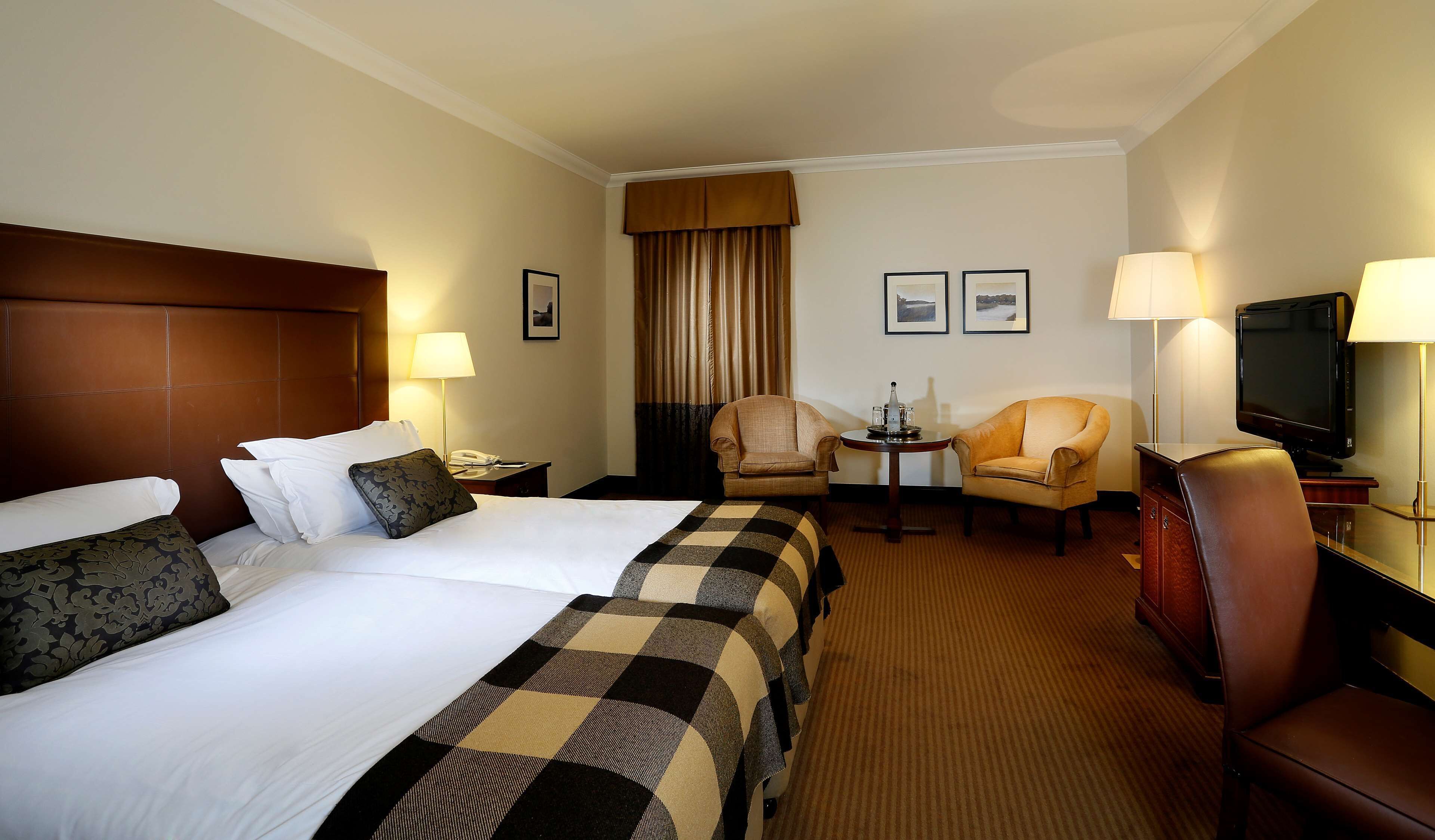 A hotel room with two beds, a TV, a desk with a lamp, and a chair.