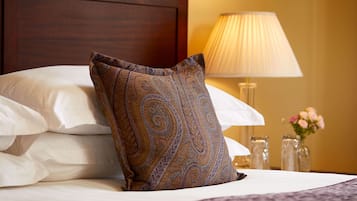A neatly made bed with a patterned pillow, a bedside lamp, and a vase with flowers.