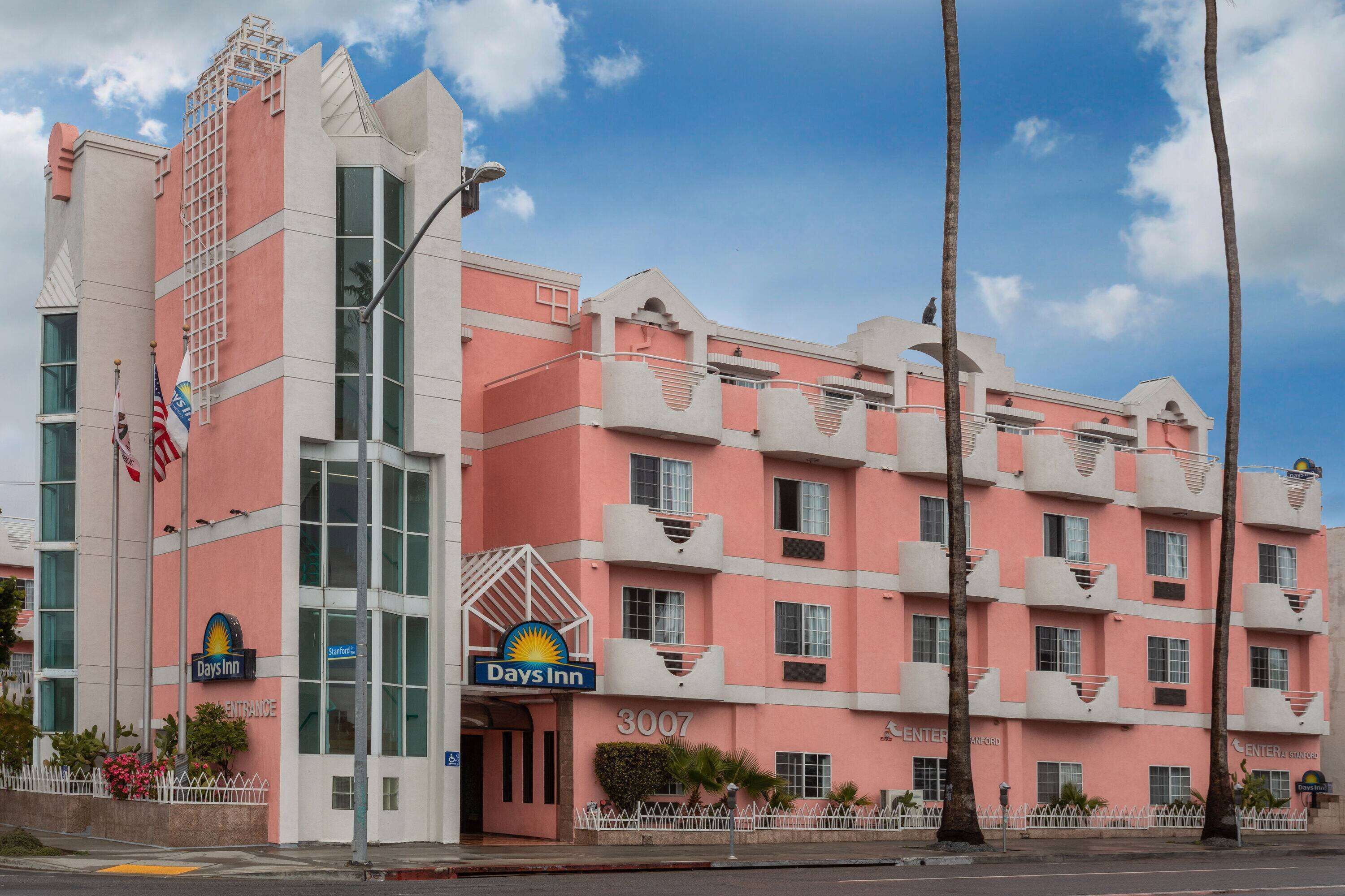A pink and white hotel with a Days Inn sign, multiple balconies, and a clear sky.