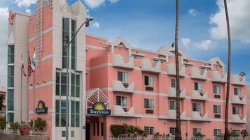A pink and white hotel with a Days Inn sign, multiple balconies, and a clear sky.