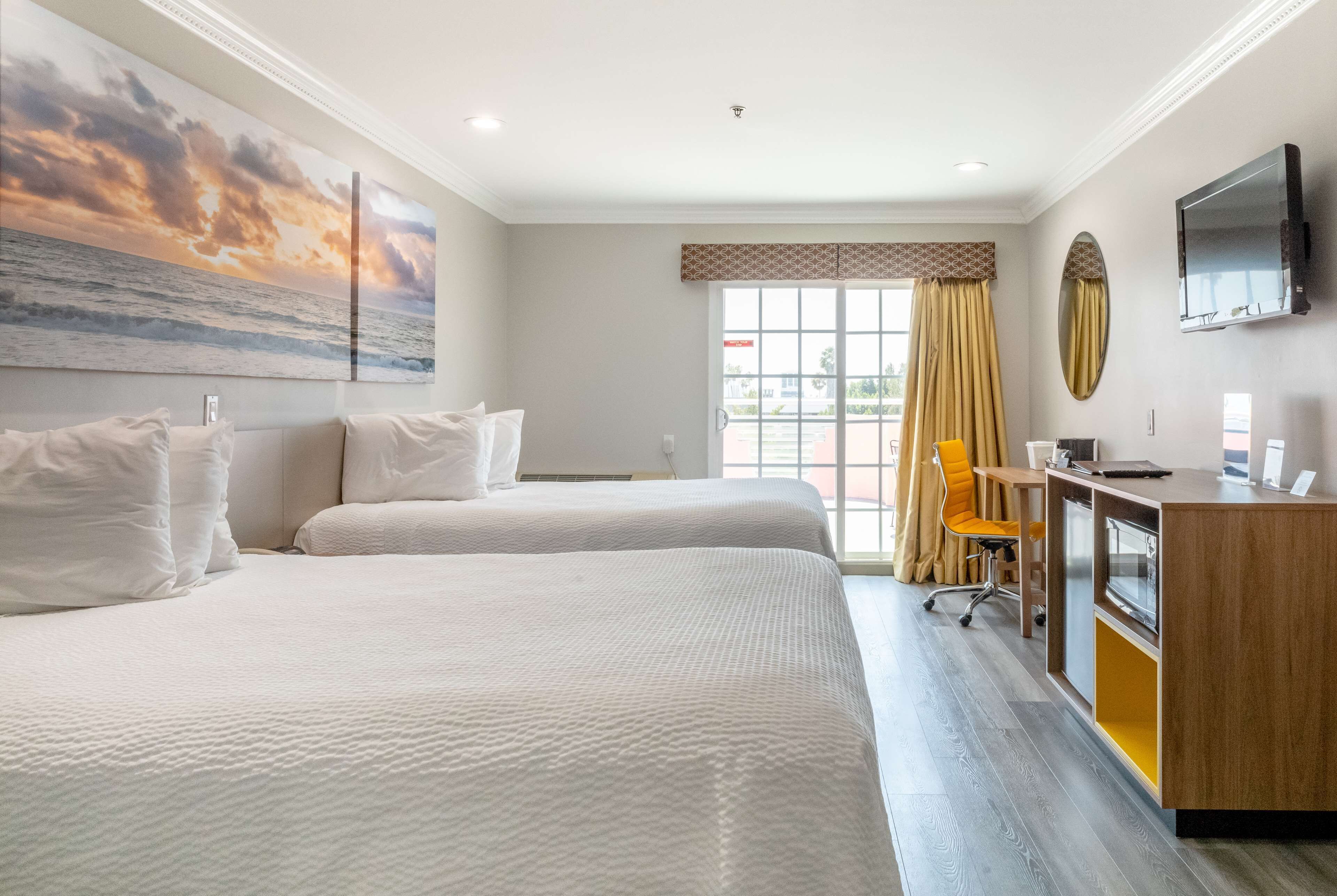 Une chambre d’hôtel avec deux lits, un bureau avec un ordinateur, une télévision et une grande fenêtre avec des rideaux.