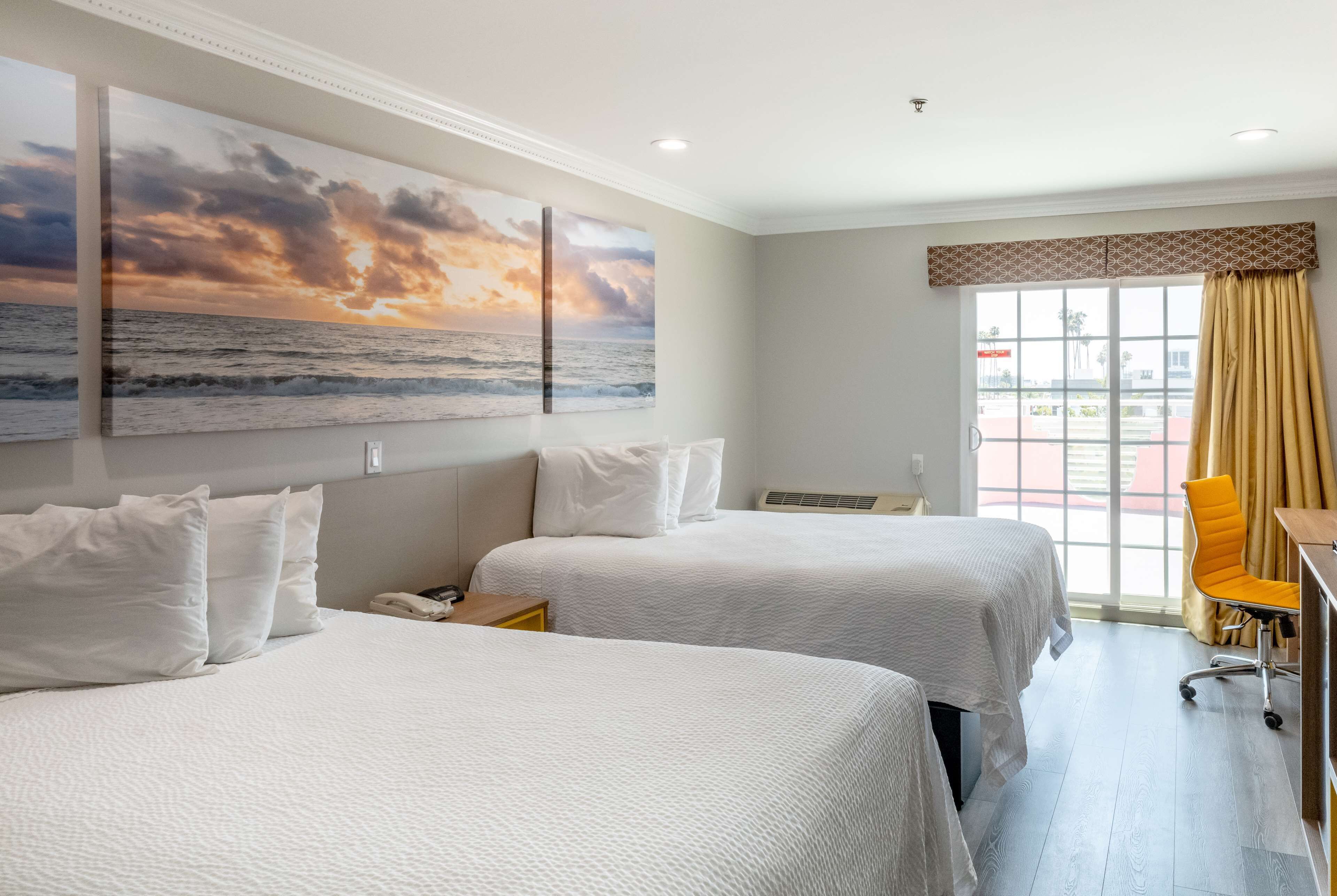 A hotel room with two beds, a large window with curtains, a desk, and a chair.