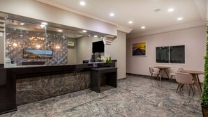 Zona d'admissió d'hotel amb sòl de marbre, taulell de recepció, televisor i àrea d'estar amb cadires i taula.