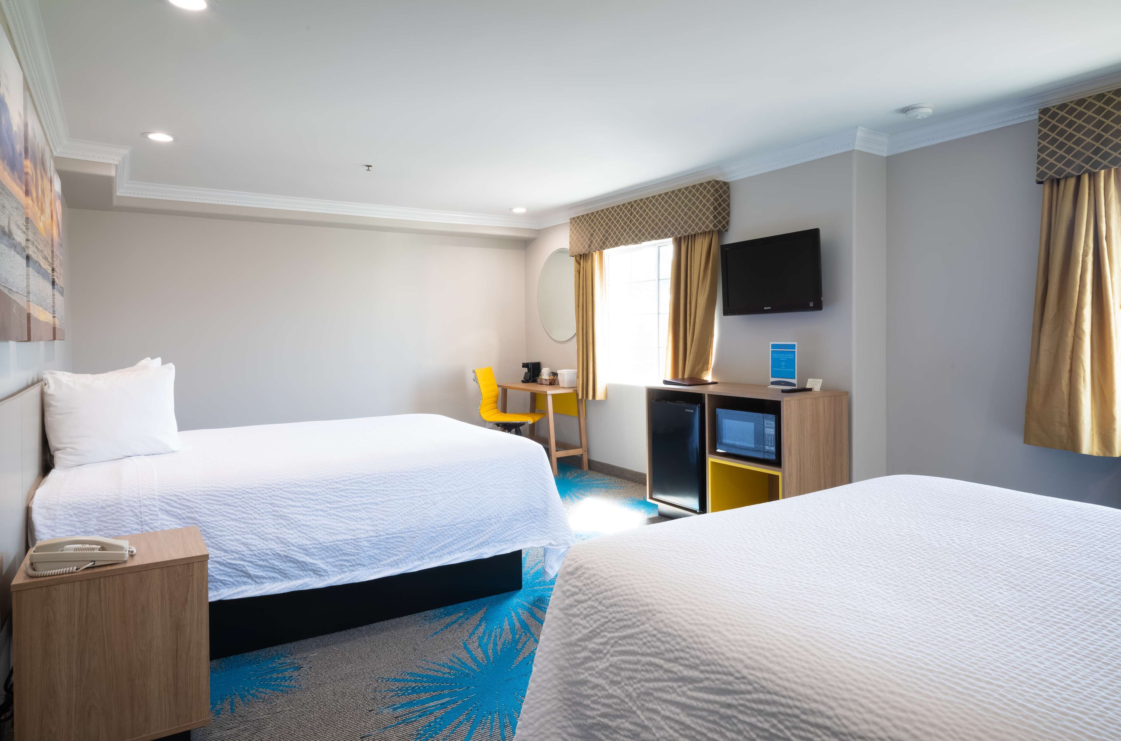A hotel room with two beds, a desk with a computer, a chair, a TV, and a small table with a phone.
