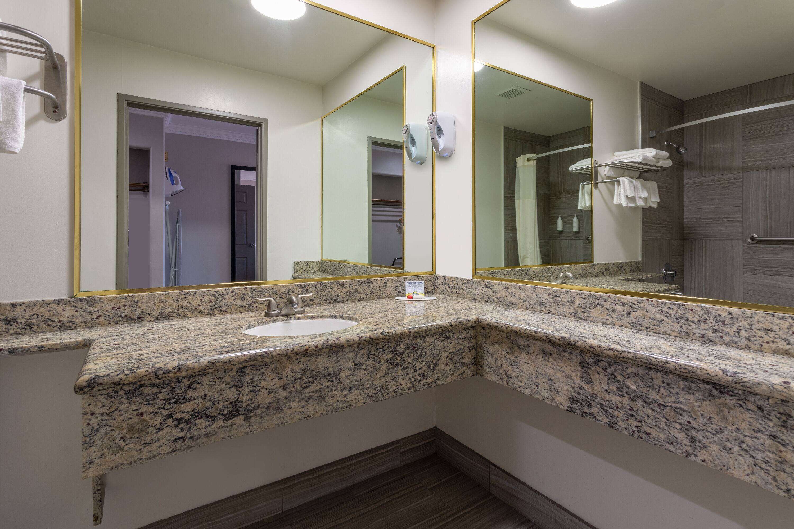 Un baño con encimeras de granito, un lavamanos, un espejo y zona de ducha.