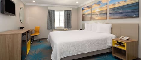 Quarto de hotel com cama, escrivaninha, cadeira, televisão e obras de arte na parede.