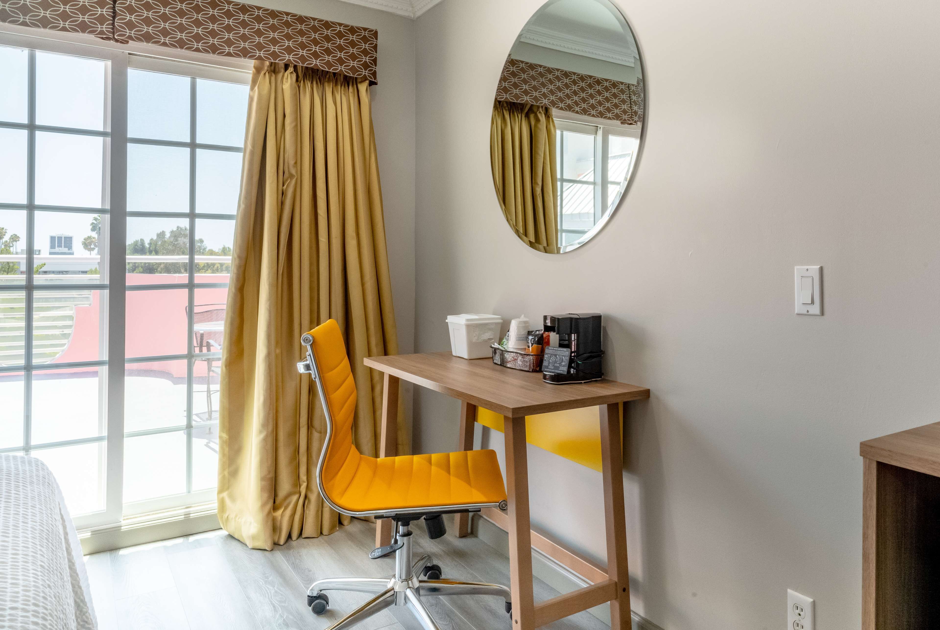 A hotel room with a large window, a yellow chair, a wooden desk, and a mirror on the wall.