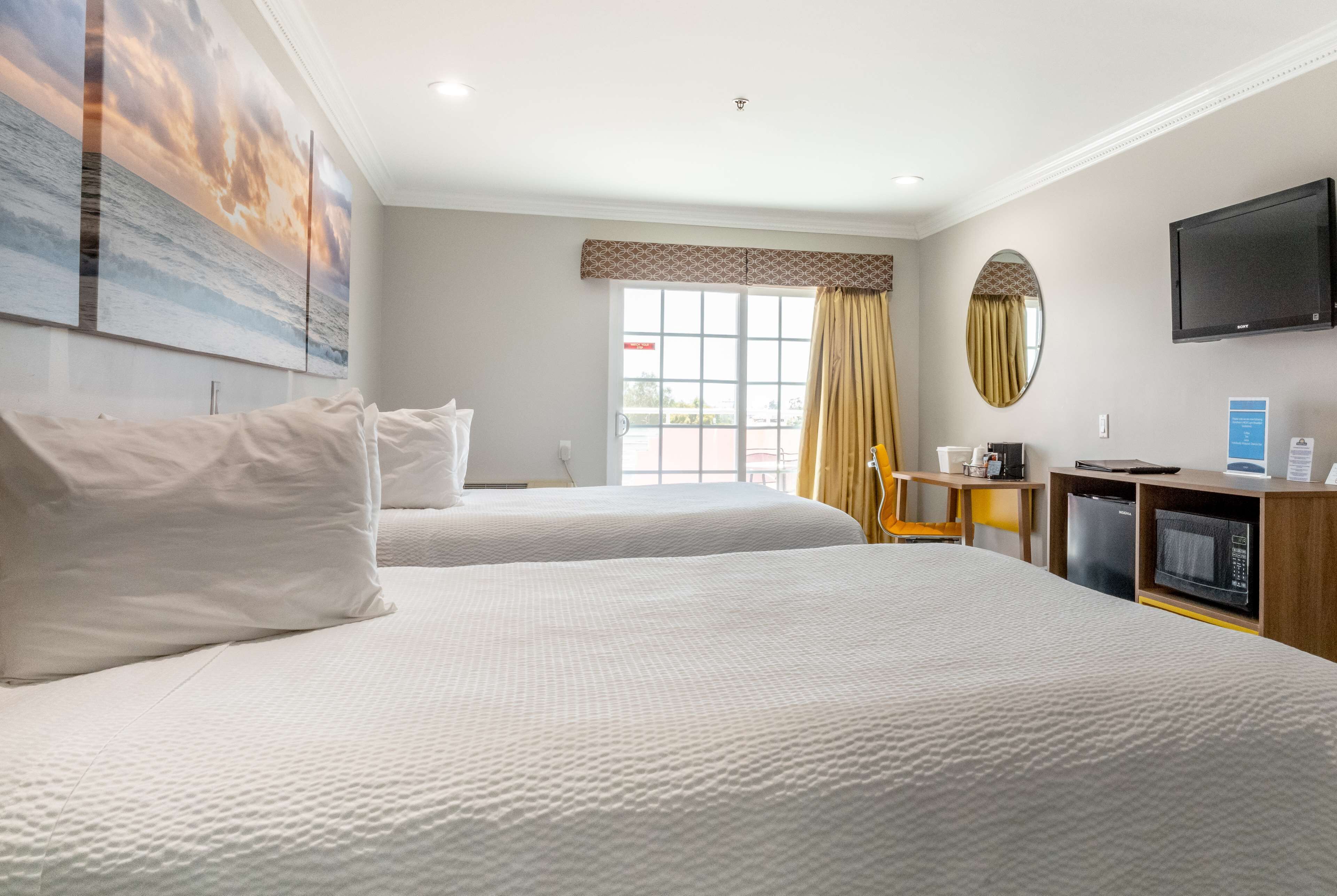 A hotel room with two beds, a desk, a television, and a view of the outdoors.