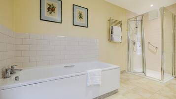 A bathroom with a white bathtub, a glass shower enclosure, and two framed pictures on the wall.