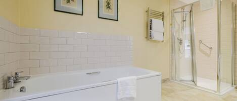 A bathroom with a white bathtub, a glass shower enclosure, and two framed pictures on the wall.