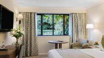 A hotel room with a bed, a desk, a chair, a round table, a TV, and a window with curtains.