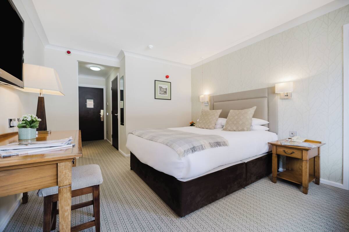 A hotel room with a large bed, bedside tables, a desk with a lamp, and a chair.