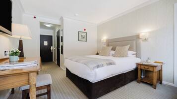 A hotel room with a large bed, bedside tables, a desk with a lamp, and a chair.