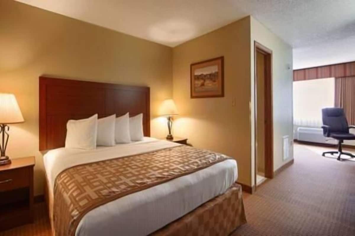 A hotel room with a large bed, two bedside tables with lamps, a chair, and a window with curtains.
