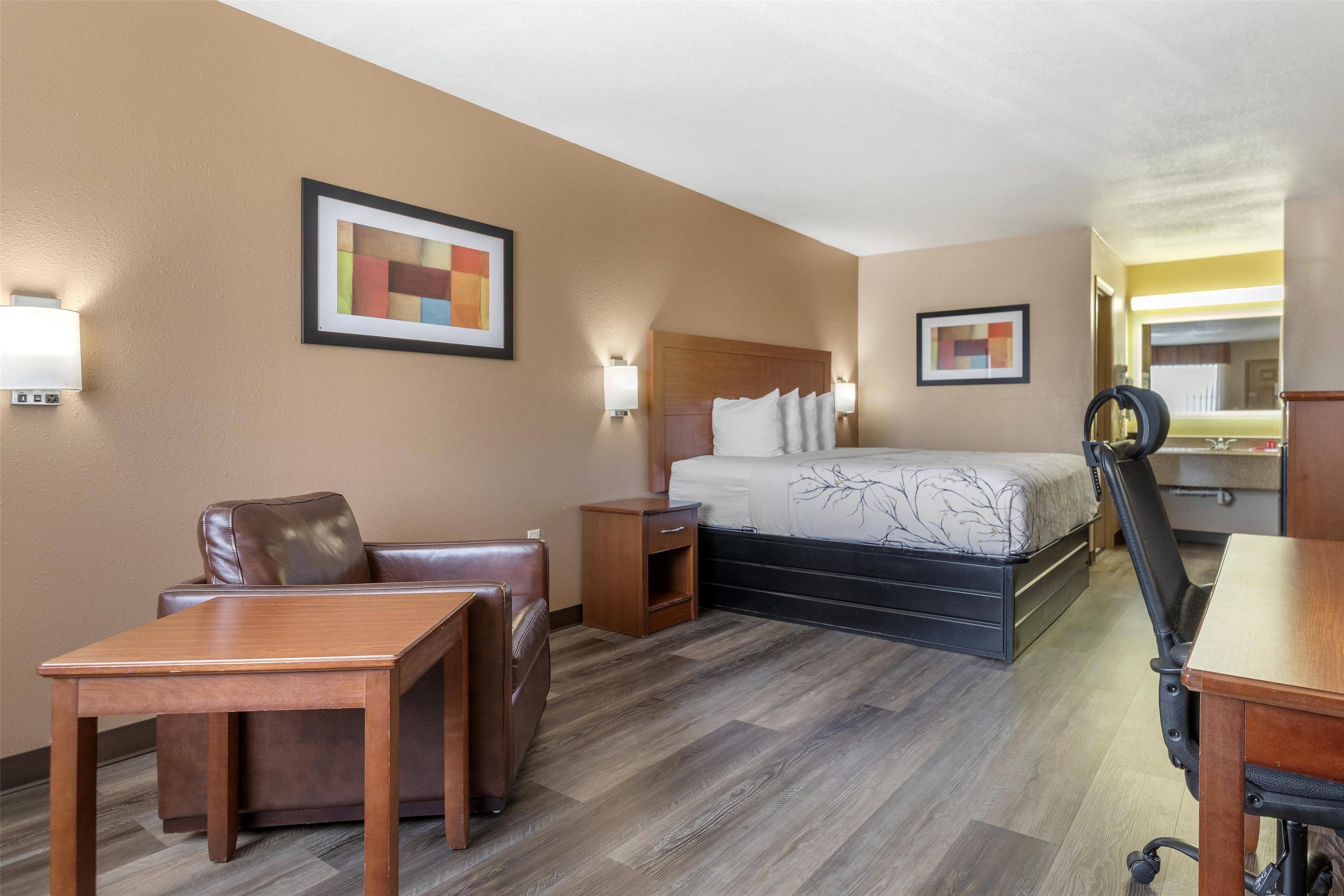Habitación de hotel con cama, escritorio, silla, mesita de noche y lámpara de pared.