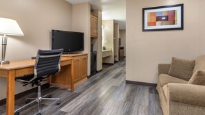 Habitación de hotel con un escritorio de madera, una silla de oficina negra, un televisor, un sofá color crema y un cuadro abstracto en la pared.
