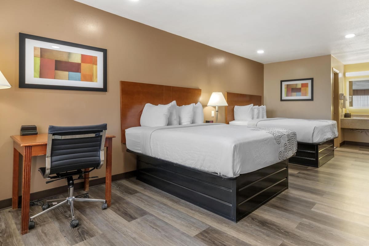 A hotel room with two beds, a desk, and a chair.