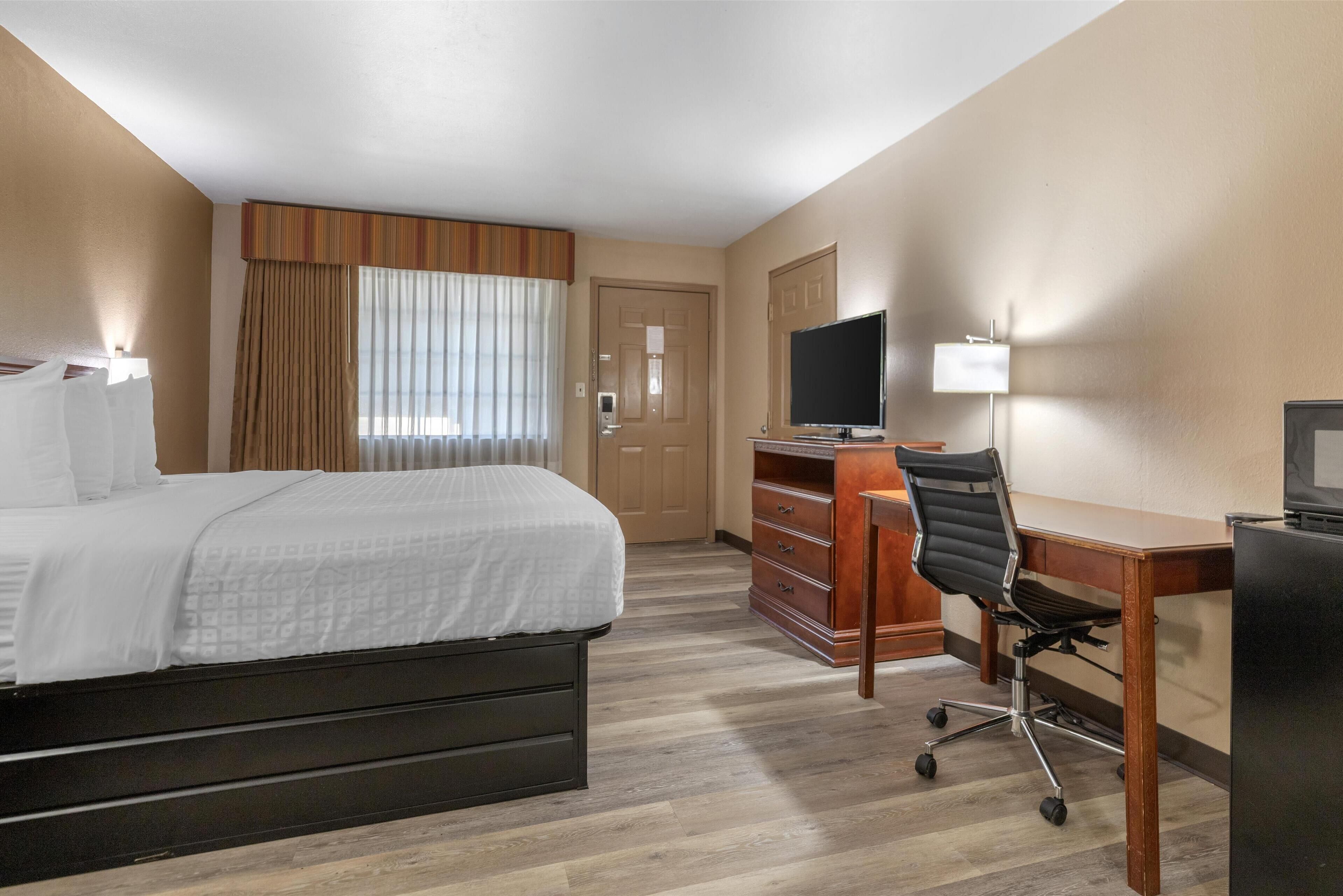 A hotel room with a bed, a desk, a chair, a television, and a dresser.