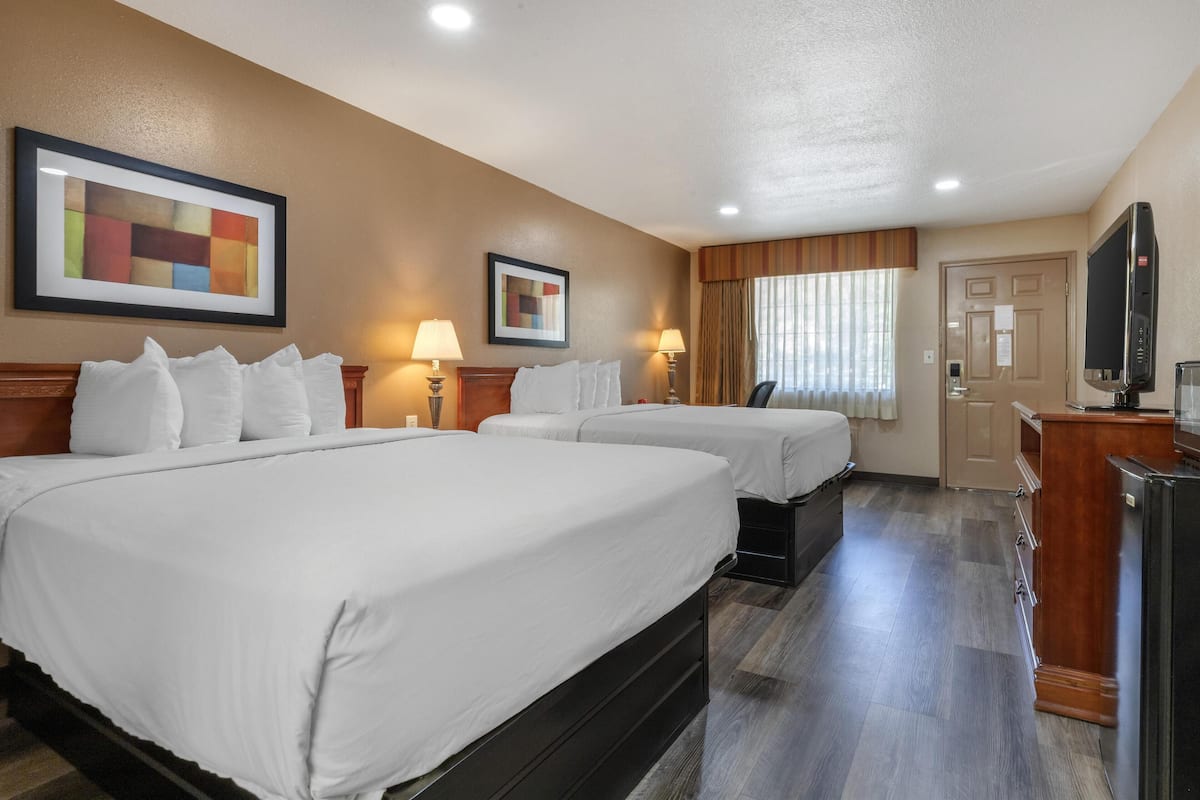 A hotel room with two beds, a desk, a television, and artwork on the walls.