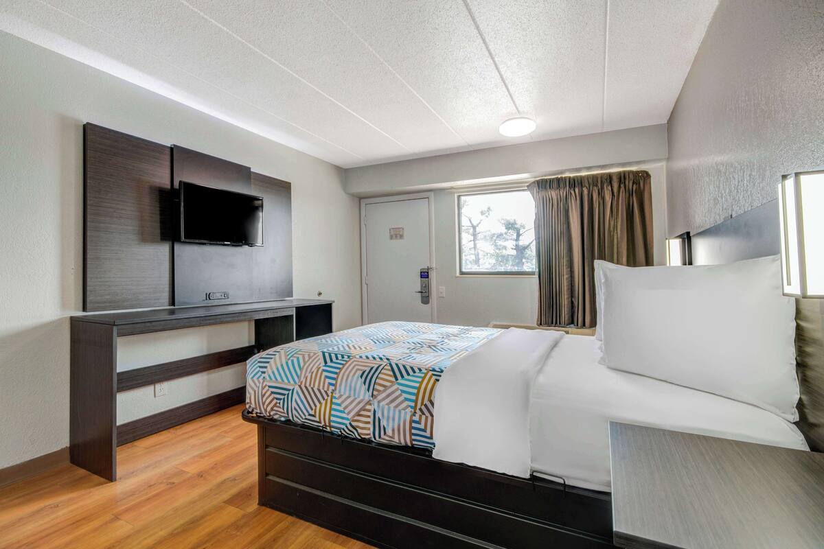 A hotel room with a bed, a TV mounted on the wall, a window with curtains, and a door.