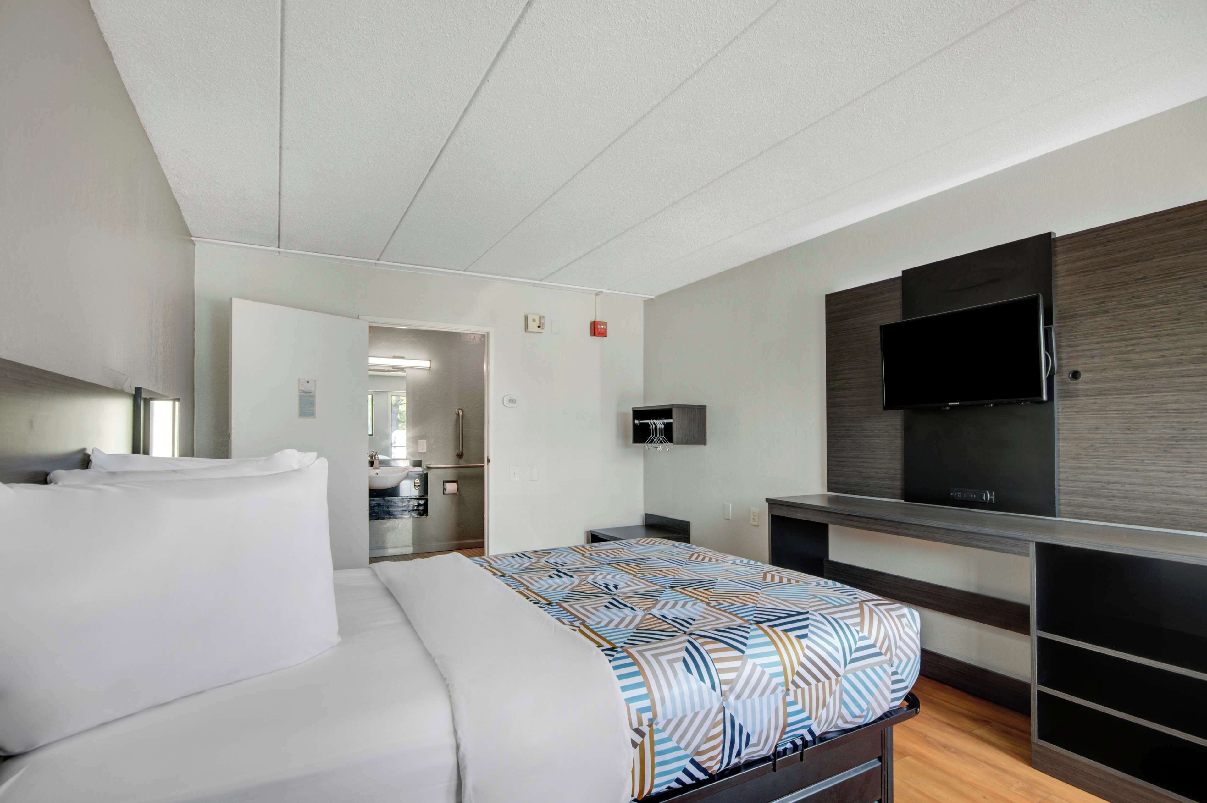 Una habitación de hotel moderna con una cama grande, un televisor de pantalla plana en la pared y una zona de kitchenette.
