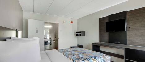 Una habitación de hotel moderna con una cama grande, un televisor de pantalla plana en la pared y una zona de kitchenette.