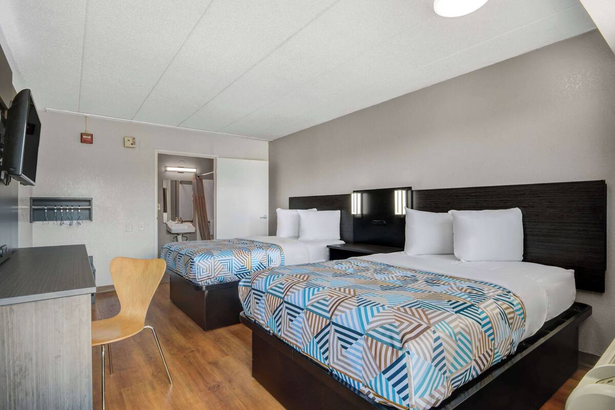 A hotel room with two beds, a desk, a chair, a TV, and a bathroom.