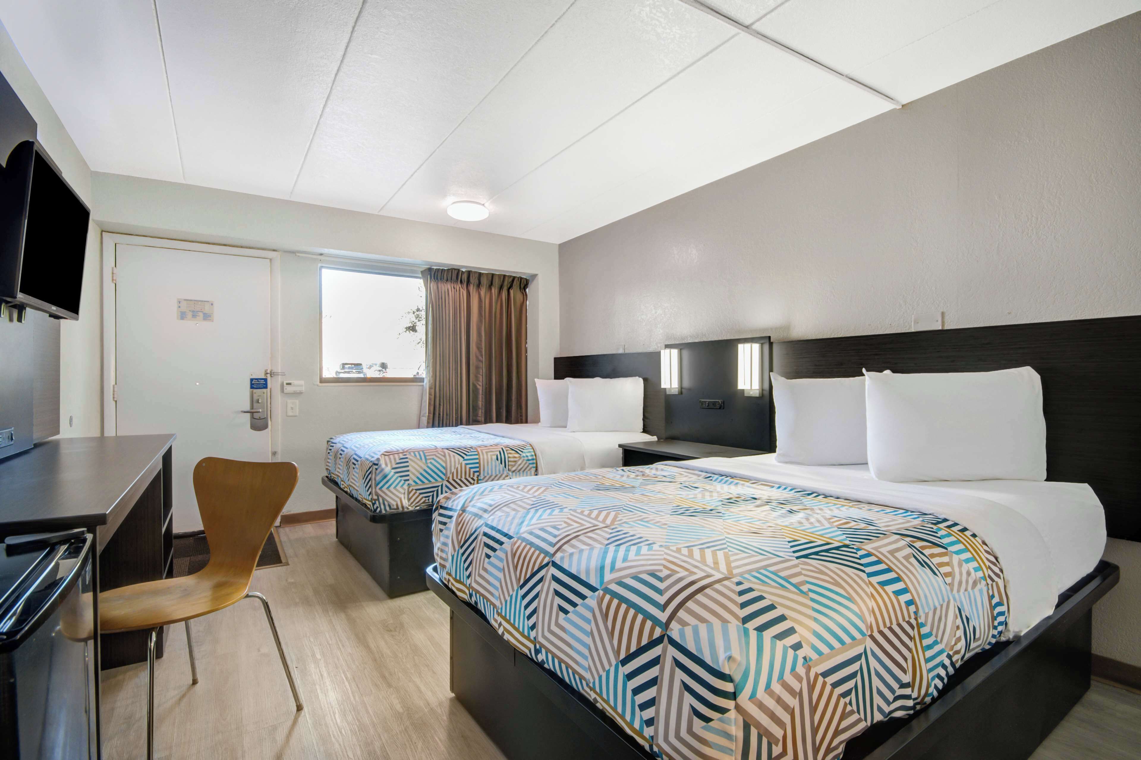 A hotel room with two beds, a desk, a chair, and a television.