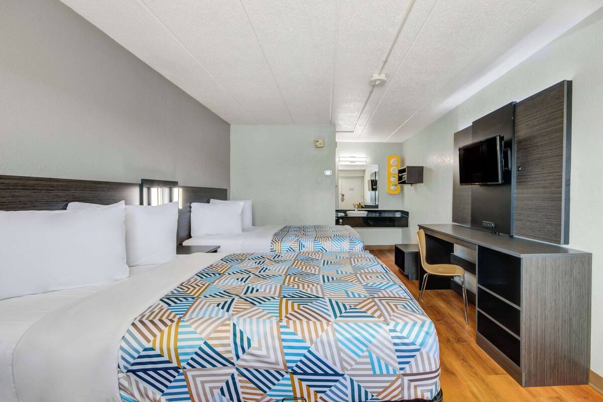 A hotel room with a large bed, a desk with a chair, a television, and a small kitchenette.