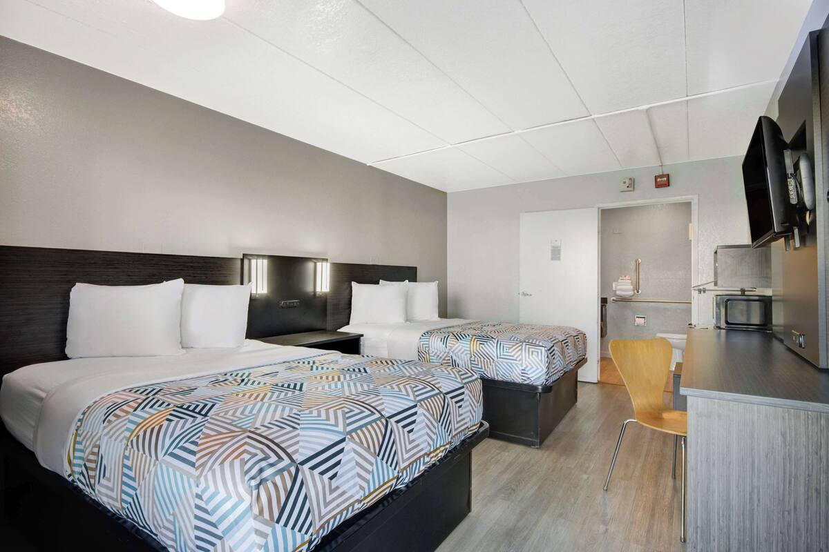 A hotel room with two beds, a small kitchenette, and a bathroom.