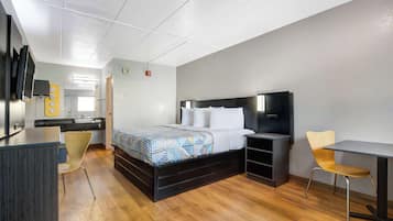 A modern hotel room with a bed, bedside table, chair, desk, and a TV mounted on the wall.