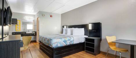 A modern hotel room with a bed, bedside table, chair, desk, and a TV mounted on the wall.