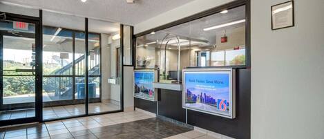 A modern lobby with glass doors, a staircase, and digital information kiosks.