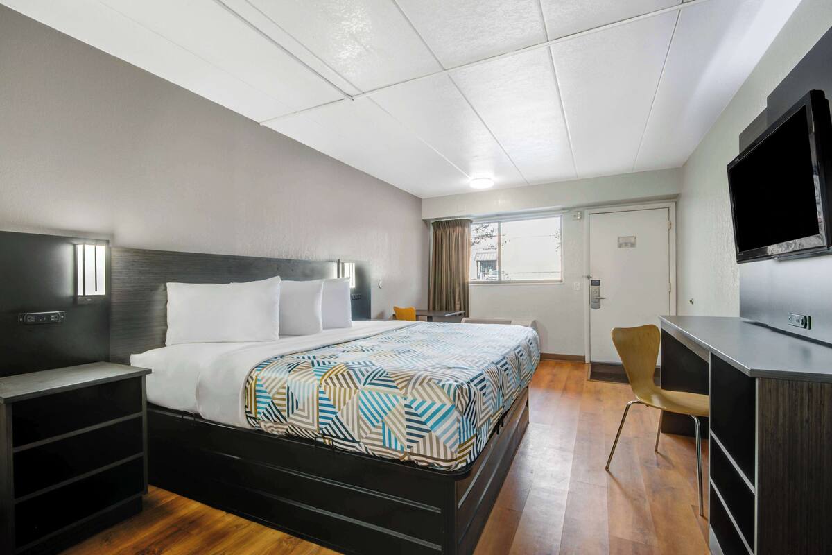 A hotel room with a bed, a desk, a chair, a TV, and a window.