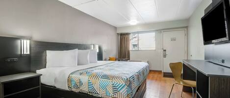 A hotel room with a bed, a desk, a chair, a TV, and a window.