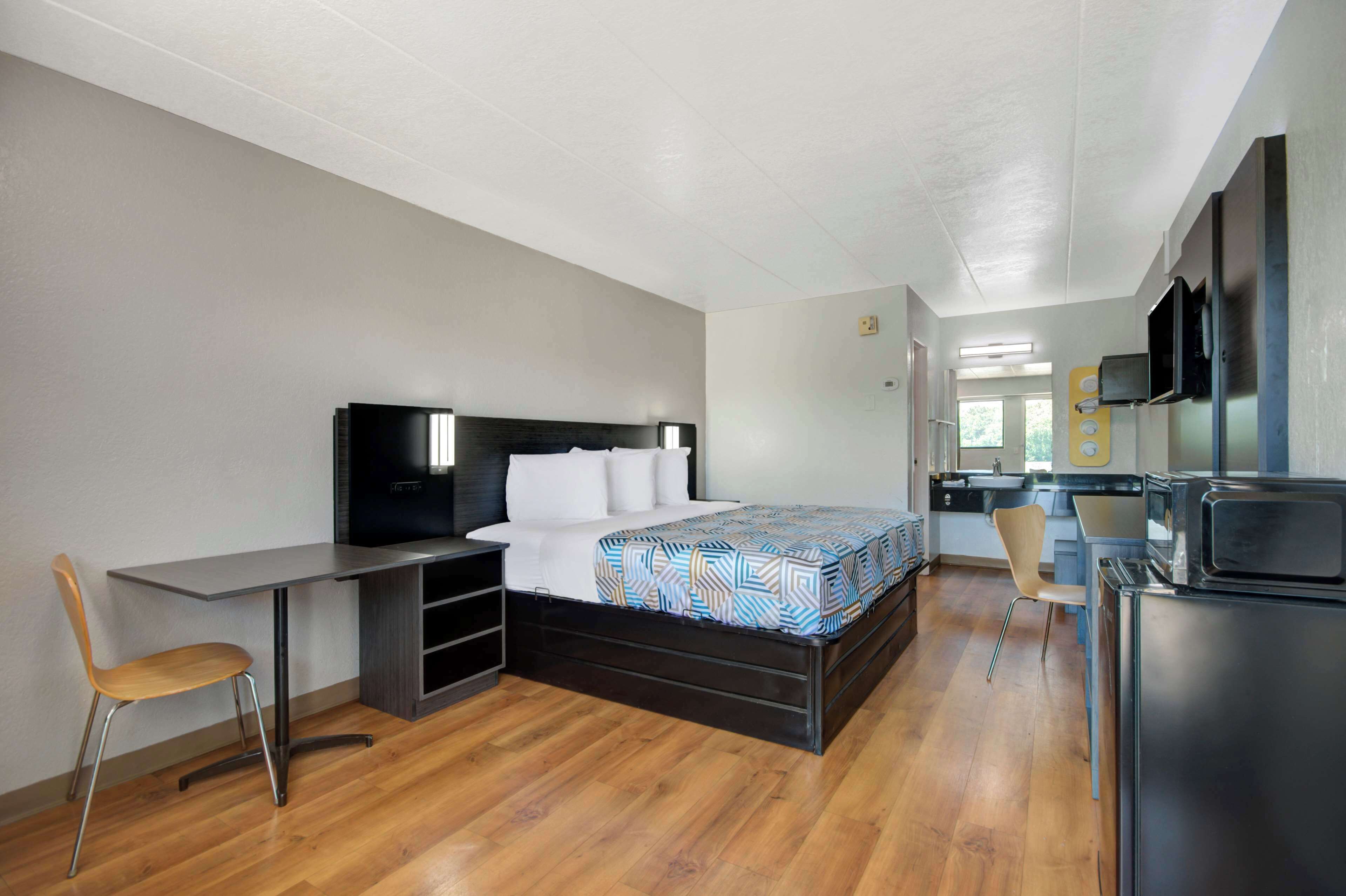 Une chambre d’hôtel de taille réduite, équipée d’un lit, d’un bureau, d’une chaise, d’une télévision et d’un réfrigérateur.