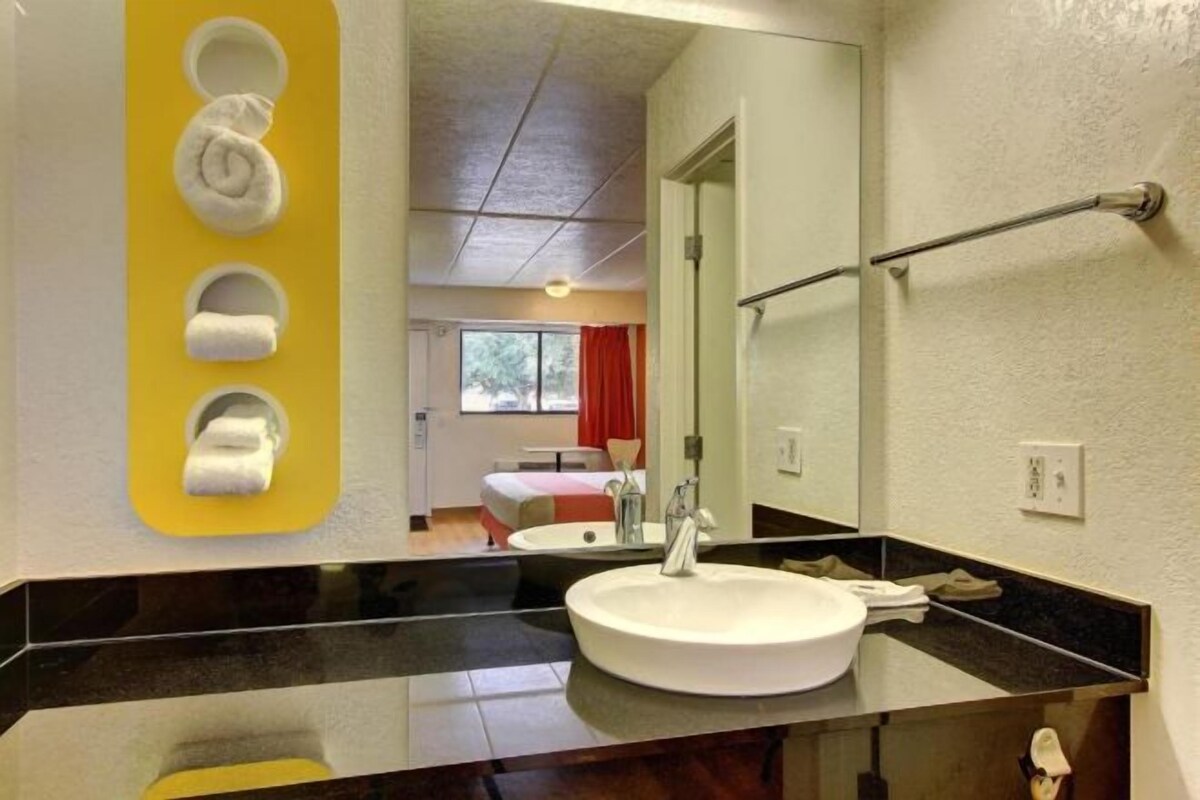 A modern bathroom with a large mirror, a round sink, and a towel rack with three towels.