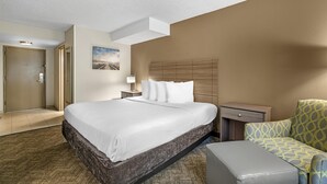 A hotel room with a large bed, a bedside table with a lamp, a chair, and a small desk. - Best Western Center Inn (Virginia Beach)