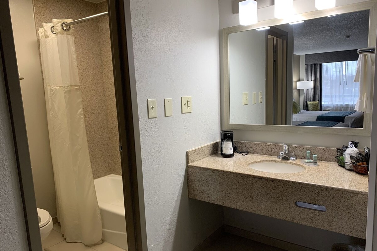 A bathroom with a shower, toilet, sink, and a large mirror.
