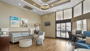 A spacious living area with a sofa, ottoman, and armchairs, a dining area with a table and chairs, and a large window with a view. - Best Western Center Inn (Virginia Beach)