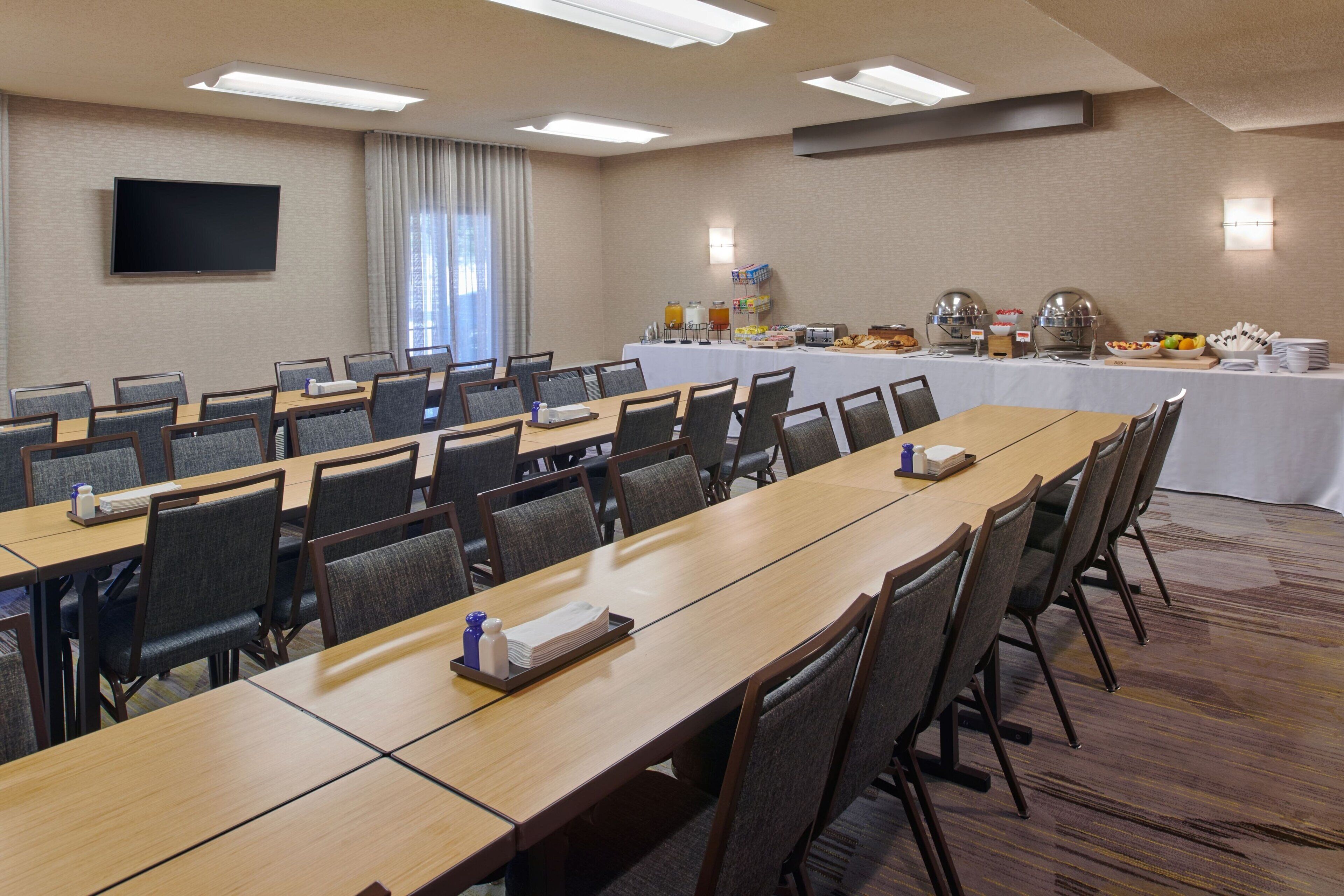A conference room with a long table, multiple chairs, a flat-screen TV, and a buffet table with various food items.