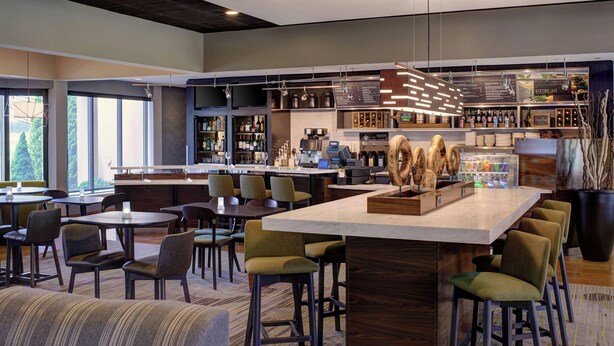 A modern bar area with a central island, bar stools, and a variety of bottles and glasses. - Courtyard by Marriott Detroit Dearborn (Dearborn)