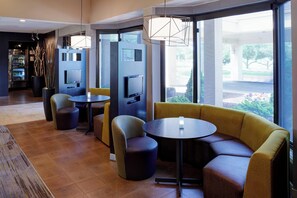 Uma área de estar moderna com sofá, poltronas e uma pequena mesa. Janelas amplas oferecem vista para o exterior.