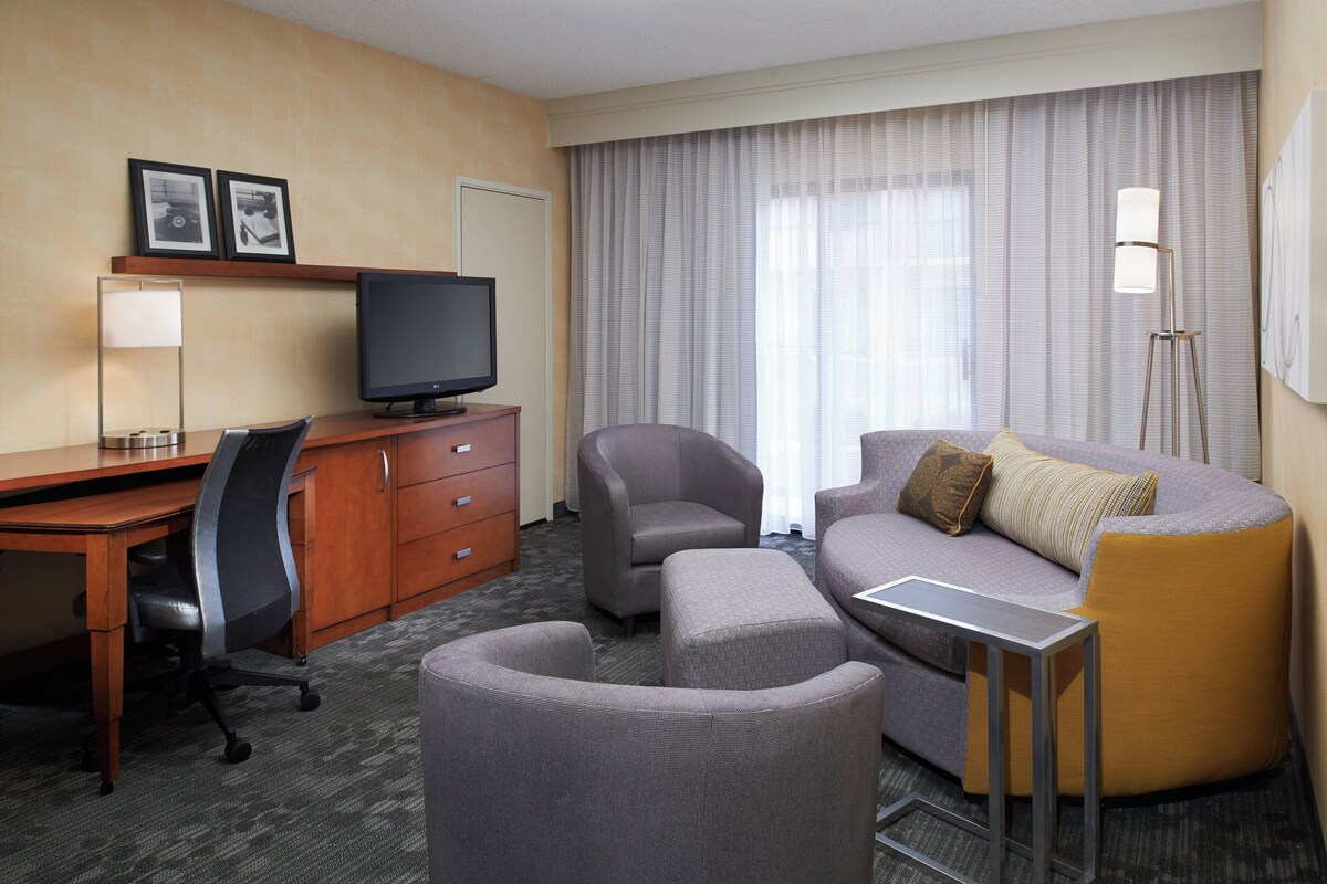 A hotel room with a desk, a television, a sofa, and a chair.