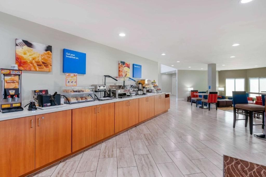 A breakfast bar with coffee machines, a food display, and seating area with chairs and tables.