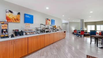 Um balcão de pequeno-almoço com máquinas de café, montra de comida e zona de estar com cadeiras e mesas.