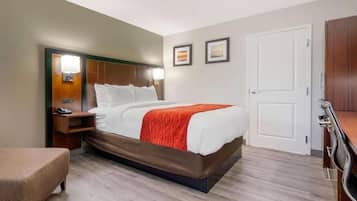 A hotel room with a bed, bedside table, lamp, and a door.