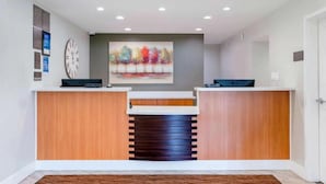 A reception area with a wooden reception desk, a clock, and a colorful abstract painting on the wall.